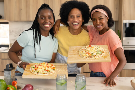African friends in colorful T-shirts smiling, holding wooden boards with pizzas on marble island
