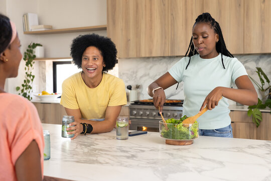 African American friends chatting while tossing salad on marble kitchen island with phone nearby