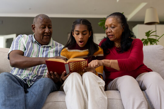 African American family reading red book on sofa, right wearing red top, pointing