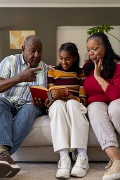African American grandparents and granddaughter sitting on sofa reading patterned hardcover book