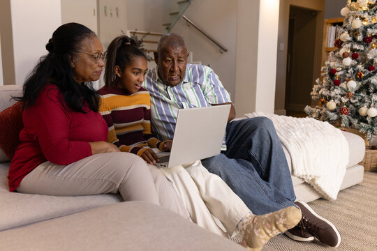 African American family with youth and senior members sitting on sectional sofa using silver laptop