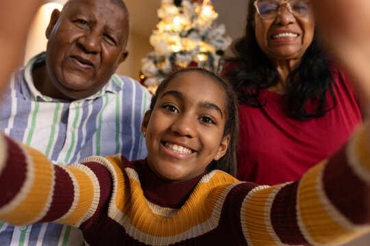 African grandparents, teen granddaughter taking selfie with phone in living room by Christmas tree