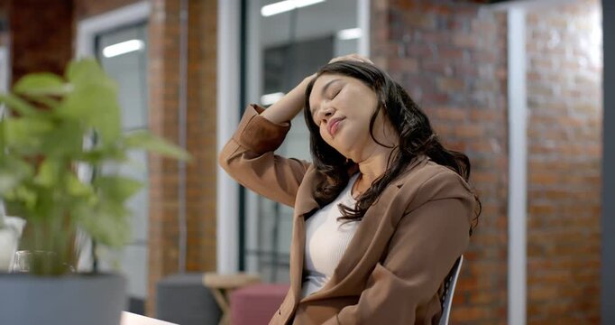 Woman in brown blazer feeling neck tension, leaning and massaging neck, typing on laptop at desk