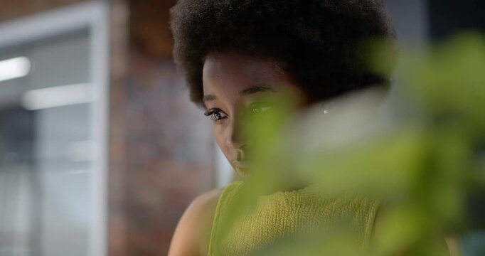 Adult African American woman reading laptop, looking smiling laughing by plant in office in yellow