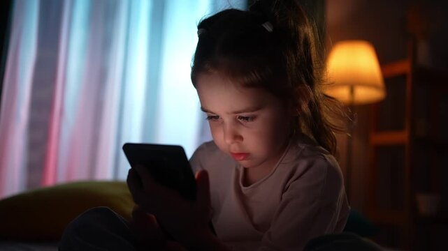 The face of a child using a smartphone in a dark room