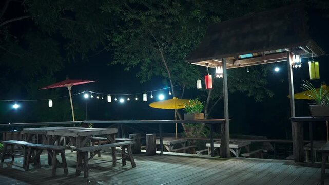 Cozy wooden village cafe terrace at night with illuminated lanterns and rustic outdoor seating, Peaceful tropical restaurant deck with warm lighting, relaxing countryside atmosphere 4k