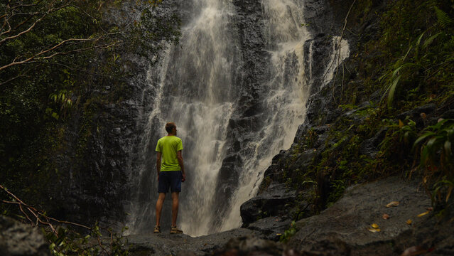 Person standing in front of a large waterfall in the Hawaiian jungle