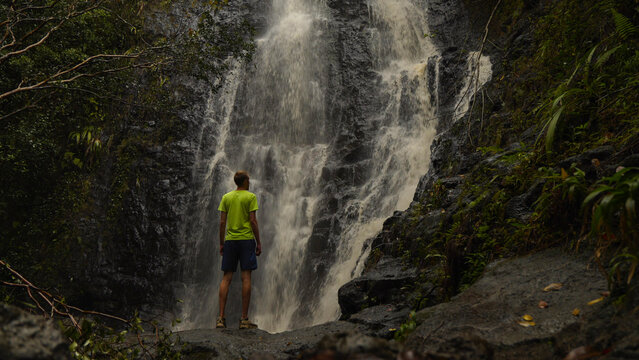 Person standing in front of a large waterfall in the Hawaiian jungle