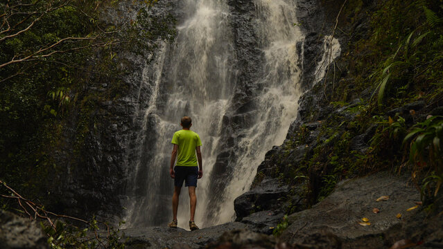 Person standing in front of a large waterfall in the Hawaiian jungle