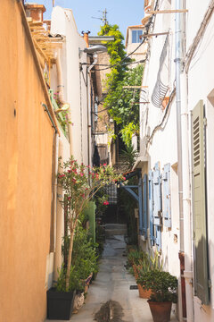 Marseille, France - 1 August 2026 : Narrow, sunlit alleyway in Vallon des Auffes, framed by pastel-colored walls, traditional blue and green wooden shutters, and potted plants.