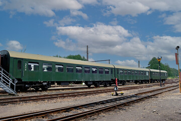A perspective view of multiple classic green passenger train coaches sitting on a network of railroad tracks at a maintenance depot under a bright blue sky. © Констянтин Батыльчук