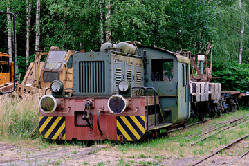 An abandoned or museum exhibit of an old green narrow-gauge diesel locomotive sitting on railway tracks surrounded by trees and green grass. © Констянтин Батыльчук