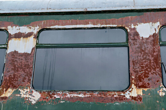 A close-up shot showing the weathered window of an old abandoned train car, featuring rusty green metal and peeling paint textures.