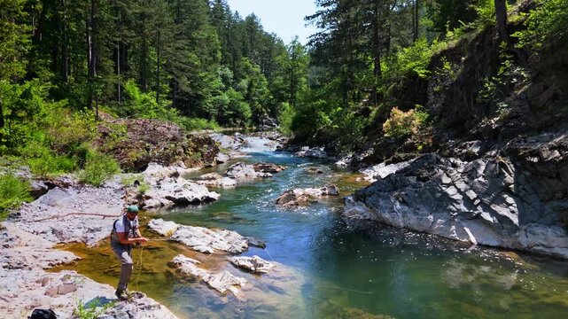 Cinematic aerial shot of angler fly fishing in rushing emerald river water surrounded by canyon walls Bosnia