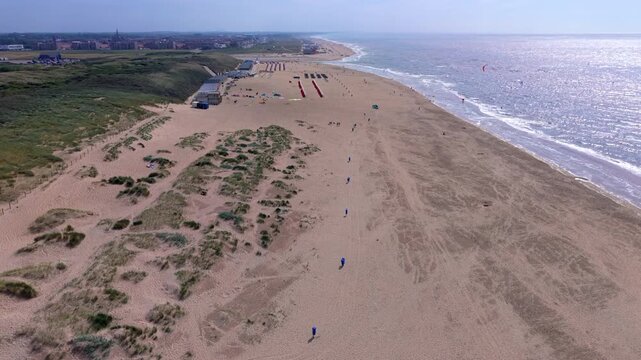 Aerial view video clip of Katwijk aan Zee sandy beach shoreline, kitesurfers in North Sea, beach cabins, coastal sand dunes, and town view in South Holland, Netherlands