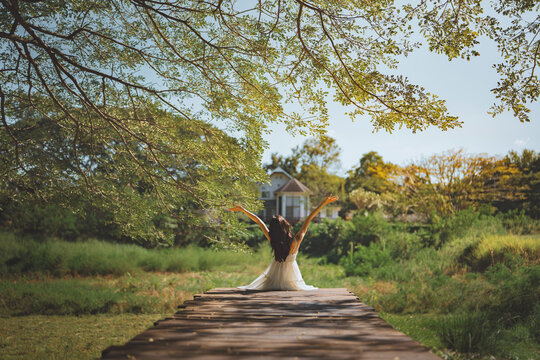 Woman sitting on wooden walkway with arms raised in peaceful green nature, freedom, relaxation and mindful outdoor lifestyle