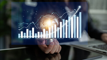 Businessman presents a light bulb symbolizing ideas and innovation, paired with financial growth graphs, showcasing the connection between creativity and market success. Impute © InfiniteFlow