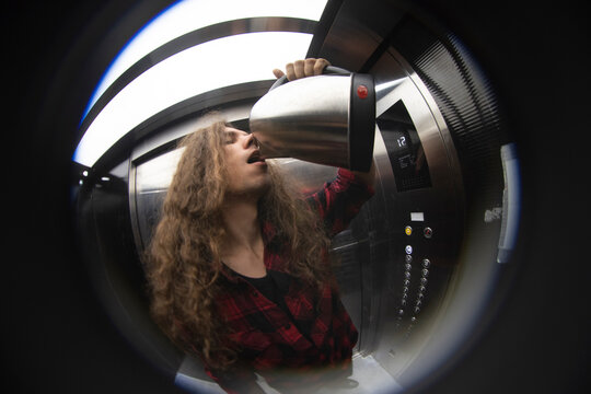 Crazy young man drinking water from electric kettle inside lift with copy space