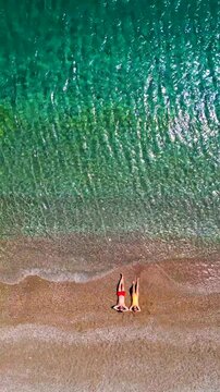 Couple in swimsuits lay on a sandy beach, top down view. Vertical