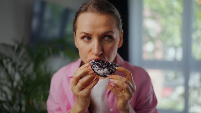 Woman eating a donut and looking around to make sure no one is watching