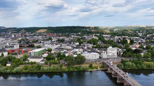Zeitraffer (Timelapse)  Drohnenaufnahme von Trier mit der antiken R&ouml;merbr&uuml;cke &uuml;ber die Mosel, umgeben von Stadtarchitektur und gr&uuml;nen H&uuml;geln unter bew&ouml;lktem Himmel an einem Sommertag.