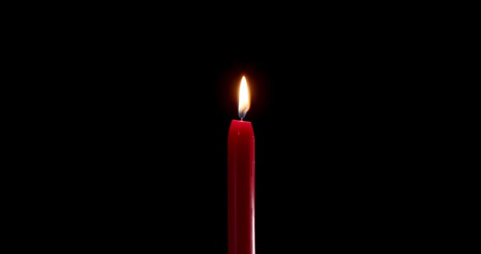 A single red candle burning on a dark, isolated background. This festive candle shines with a bright, clean flame of hope. Perfect candle for stock layouts with blending mode screen or add.
