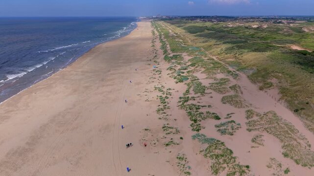 Aerial view video clip of wide sandy coastline near Katwijk aan Zee, coastal sand dunes landscape, Scheveningen distant skyline, and North Sea horizon in South Holland, Netherlands