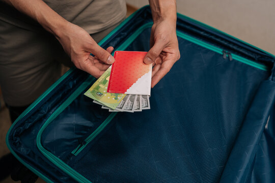 Top view of person packing passport, dollars and euro into suitcase pocket, arranging essential documents and cash preparing for upcoming international trip or vacation adventure.