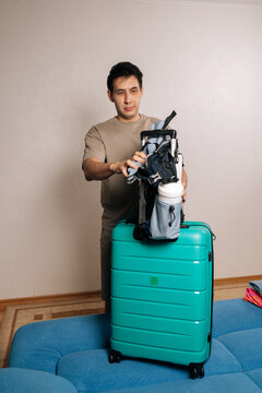 Asian man preparing luggage for vacation, attaching a travel backpack to a rolling suitcase, getting ready for an exciting journey or business trip overseas.