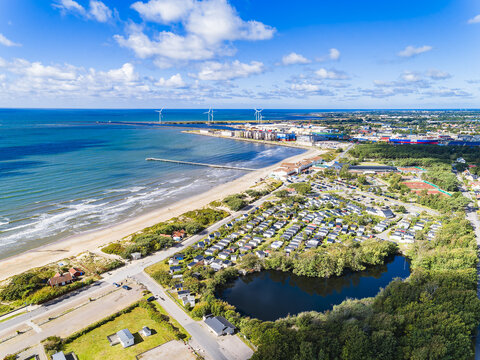 Aerial view of Skrea strand featuring a sandy beach, a large camping area with numerous caravans, a small lake, and wind turbines along the coastline in Falkenberg, Halland County, Sweden.