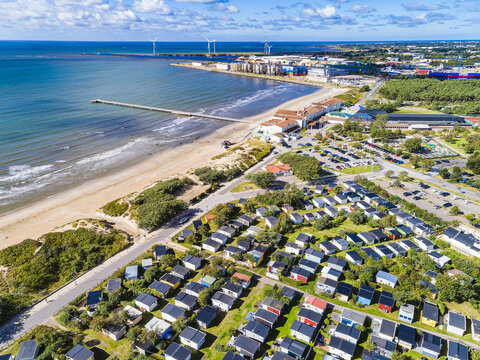 Aerial view of Skrea strand beach with its long pier, adjacent holiday park with numerous small cabins, and the coastline of the Baltic Sea in Falkenberg, Halland County, Sweden.