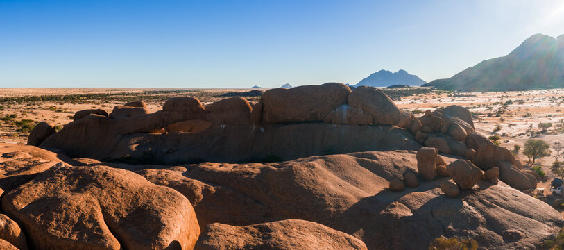 An aerial perspective captures the massive granite rock formations and expansive dry desert landscape of Spitzkoppe in Namibia under clear skies.