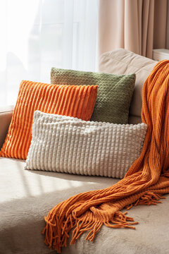 Cozy arrangement of textured sofa cushions and a knitted throw blanket in warm tones