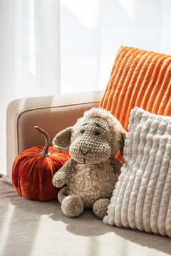 Cozy autumnal interior scene featuring plush stuffed sheep toy and decorative velvet pumpkin beside soft textured cushions for festive home decor