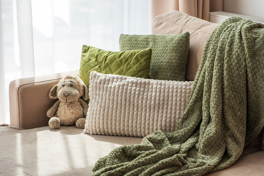 Cozy plush blanket and textured pillows arranged on a comfortable sofa with a stuffed toy