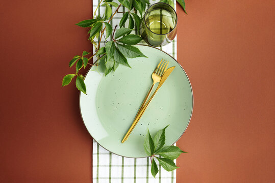 Thanksgiving Table Setting With Golden Cutlery Green Plate And Autumn Leaves On Brown Background