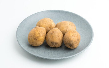 Fototapeta premium Fresh raw baby potatoes served on a grey ceramic plate isolated on white background