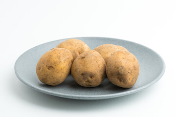 Fototapeta premium Fresh raw baby potatoes served on a grey ceramic plate isolated on white background