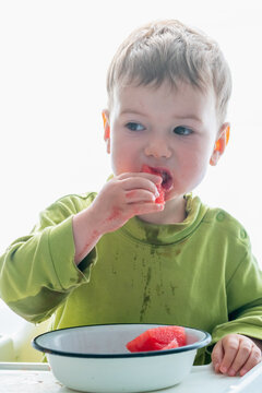 Candid unposed moment of a messy little boy naturally enjoying fresh watermelon at home.
