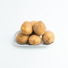 Fototapeta premium Fresh raw brown potatoes served on a blue patterned ceramic plate isolated on white background