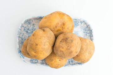 Fototapeta premium Fresh raw brown potatoes served on a blue patterned ceramic plate isolated on white background
