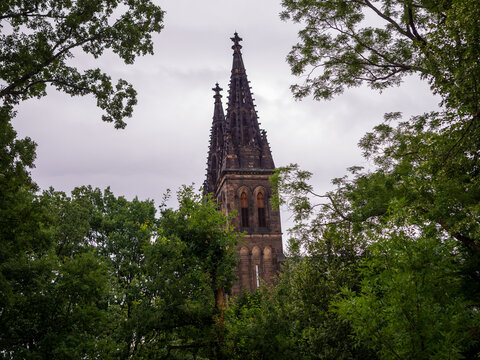 Neo-Gothic tower of the Basilica of St Peter and Paul at Vysehrad framed by lush green trees under an overcast sky in Prague, Czech Republic.