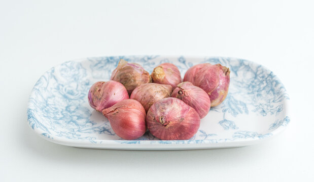 Fresh red onions shallots served on a blue patterned ceramic plate isolated on white