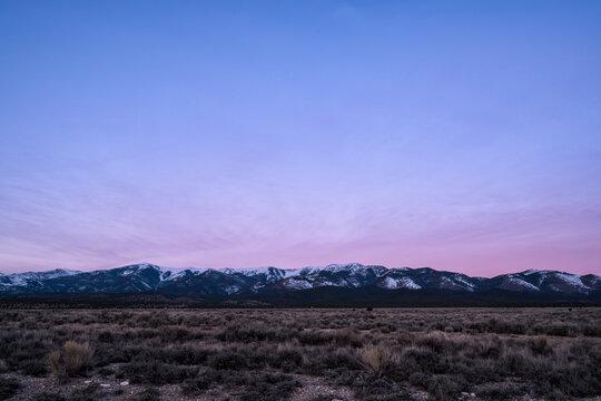 View of the snow-capped Schell Creek Range rising above the arid sagebrush plains of the Great Basin during a colorful twilight in Ely, Nevada, United States.