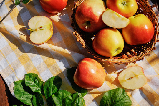 Fresh red and yellow apples in a wicker basket with sliced apples on a checkered tablecloth in a sunny garden, creating a healthy harvest and autumn lifestyle concept