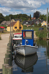 This photo shows a traditional Danish fishing boat with a distinctive blue wheelhouse, moored in a quiet harbor. © Anja