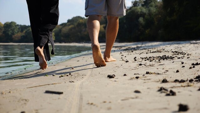 Bare feet of couple stepping together along sand beach at coastline. Male and female legs of pair walking near seaside. Happy lovers going along sandy shore. Concept of summer vacation or holiday