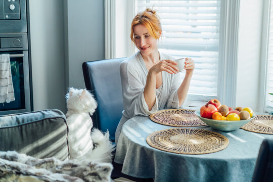 Woman, home and kitchen with cup of coffee on morning for breakfast, relax and enjoy. Middle aged female smile to cat pet, satisfied with tea to chill, fun and day off with caffeine drink and peaceful