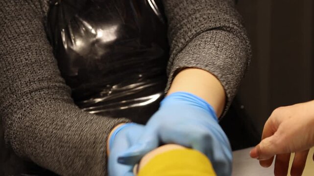 Manicurist in blue gloves giving a relaxing hand massage to a client at the end of a manicure procedure in a beauty salon. Hands receiving nourishing skin care, pampering relaxation, beauty service