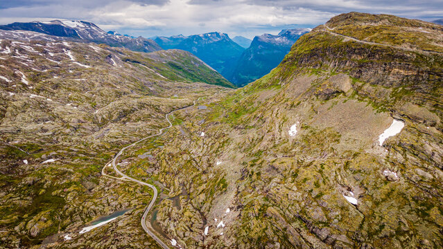 Aerial view of Djupvatnet lake surrounded by rugged mountain terrain, rocky slopes with patches of snow, and a winding road in Stranda Municipality, More og Romsdal, Norway.